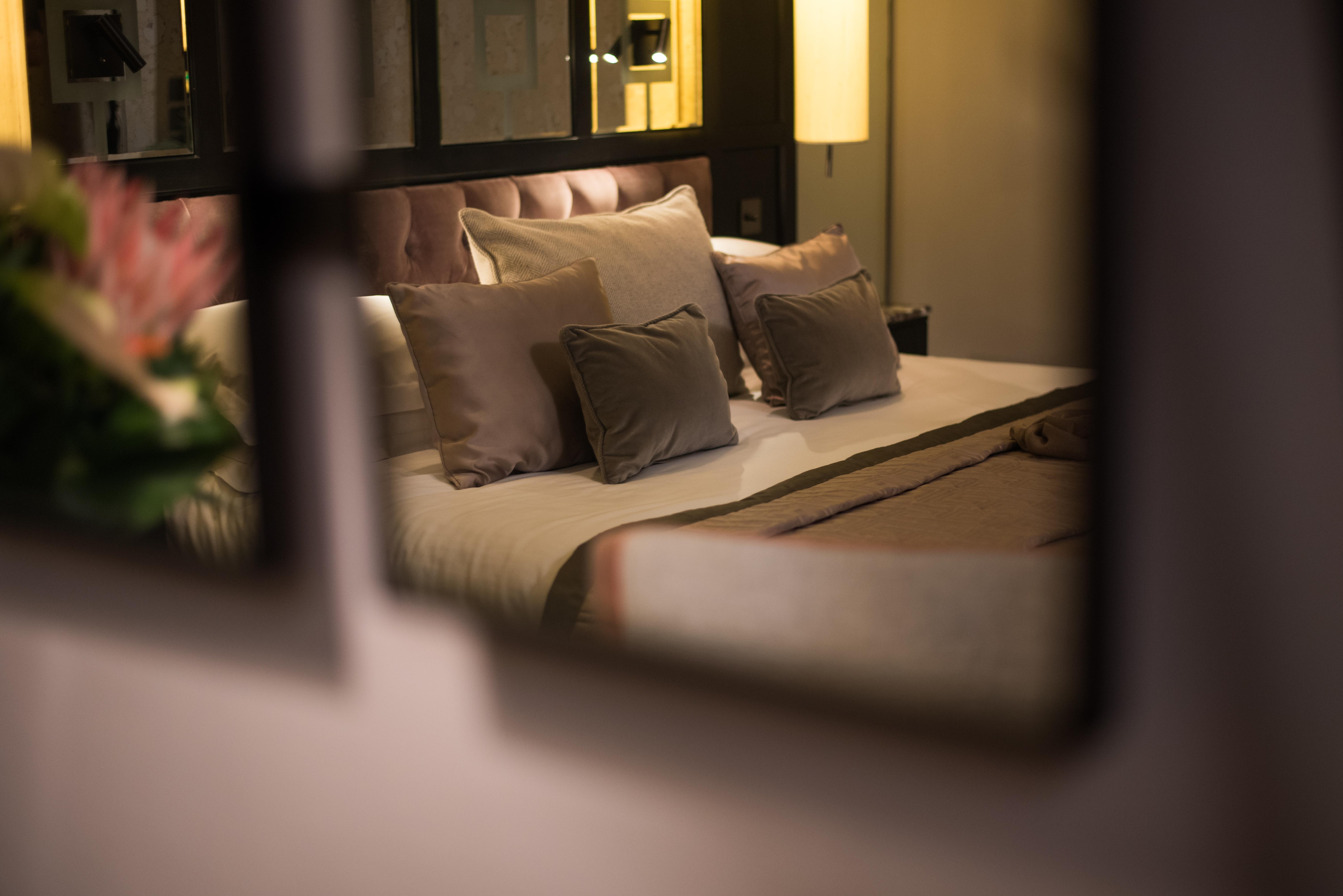 The Fitzwilliam Hotel Belfast Exteriör bild The photo shows a cozy and elegantly decorated bedroom. The focal point is a plush bed with soft, neutral-colored bedding and several decorative pillows arranged neatly on it. The room has a warm ambiance, enhanced by a standing lamp that provides so