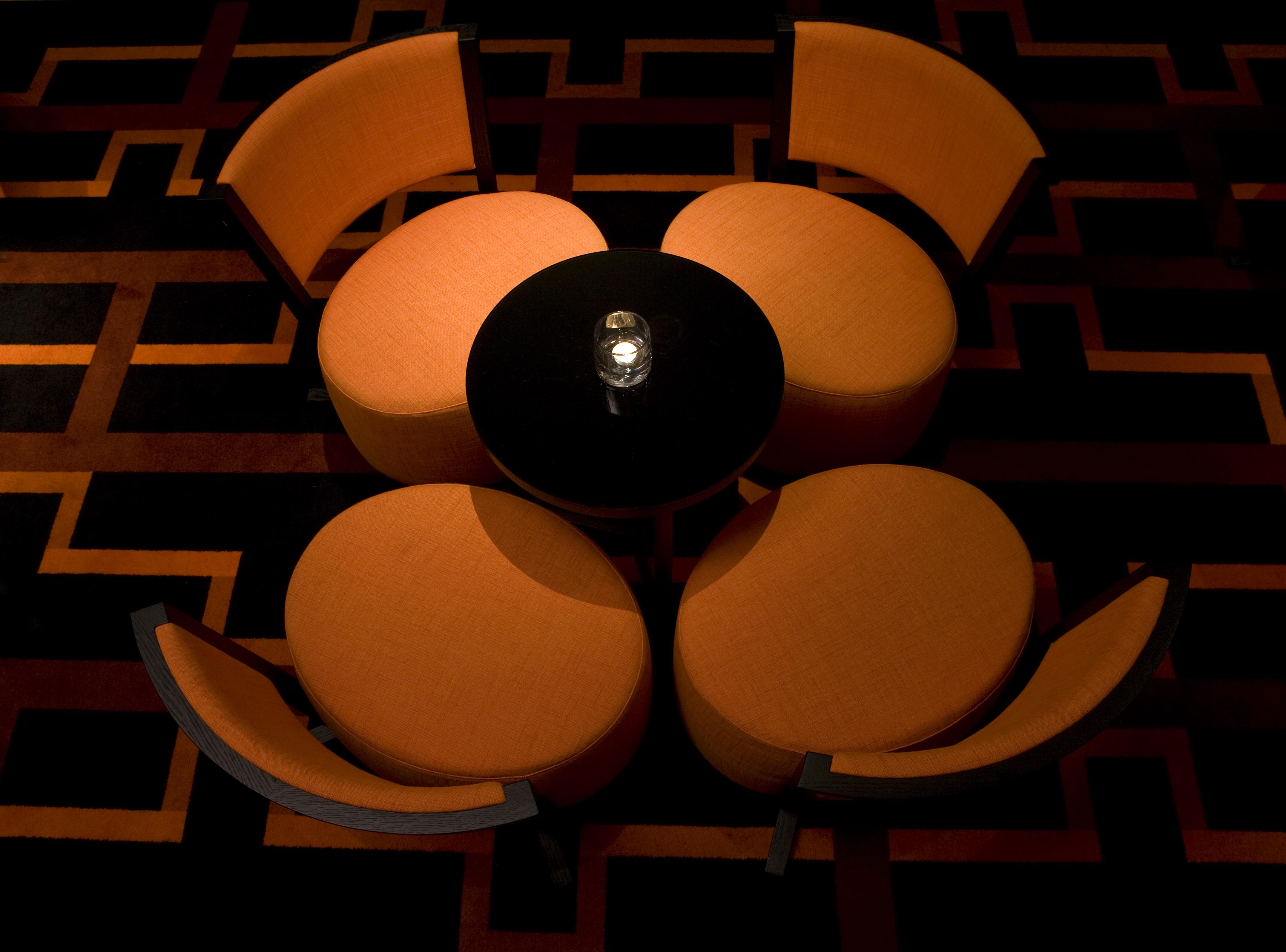 The Fitzwilliam Hotel Belfast Exteriör bild The image shows a small seating arrangement consisting of four orange chairs arranged around a circular black table. The setting appears to be in a dimly lit area, emphasizing the warm tones of the chairs and the dark finish of the table. The floor d