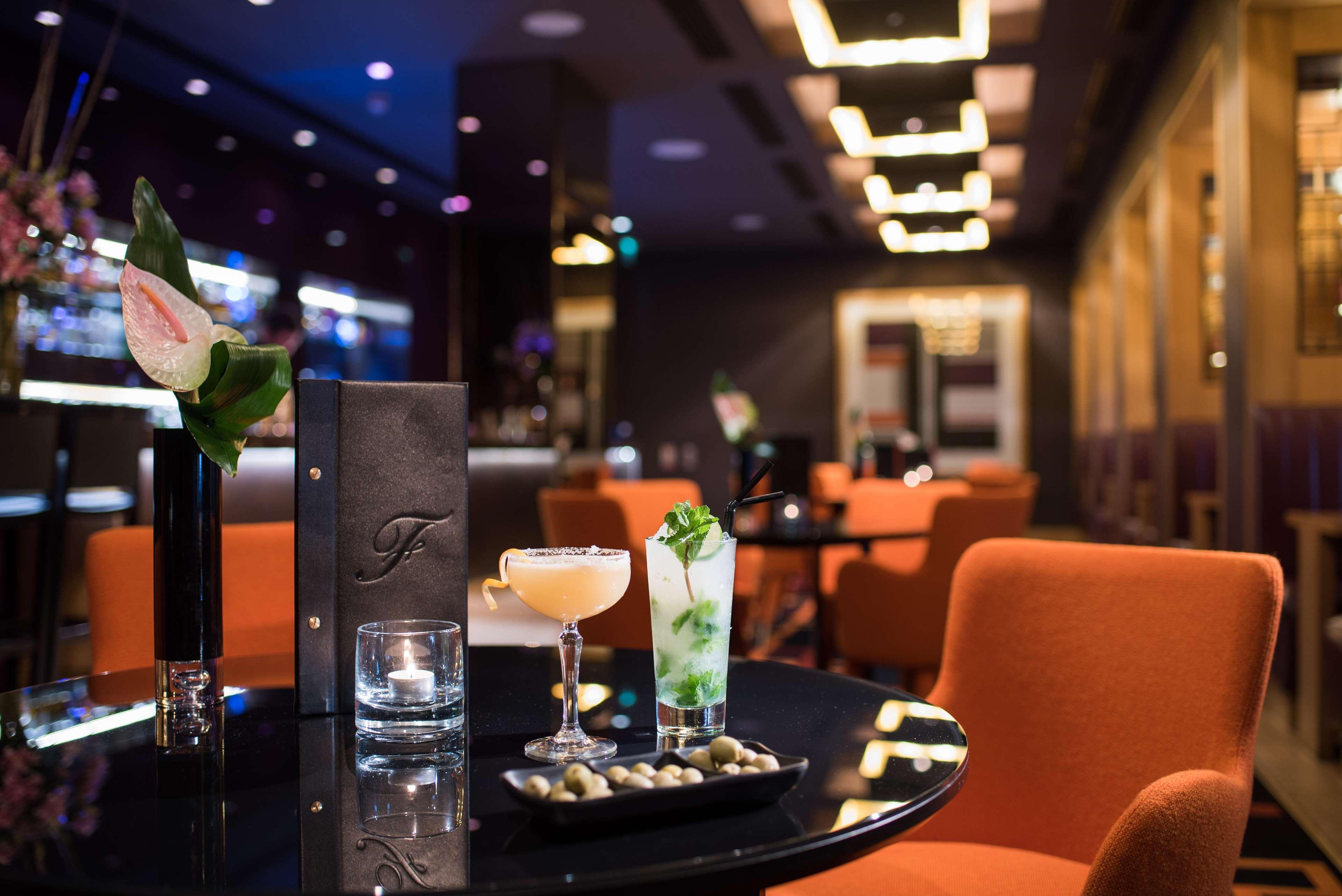 The Fitzwilliam Hotel Belfast Exteriör bild The photo depicts a stylish bar or lounge setting. There are two cocktails on a black table: one appears to be a light-colored drink garnished with a slice of fruit, while the other is a green cocktail possibly containing mint. A small plate of olive