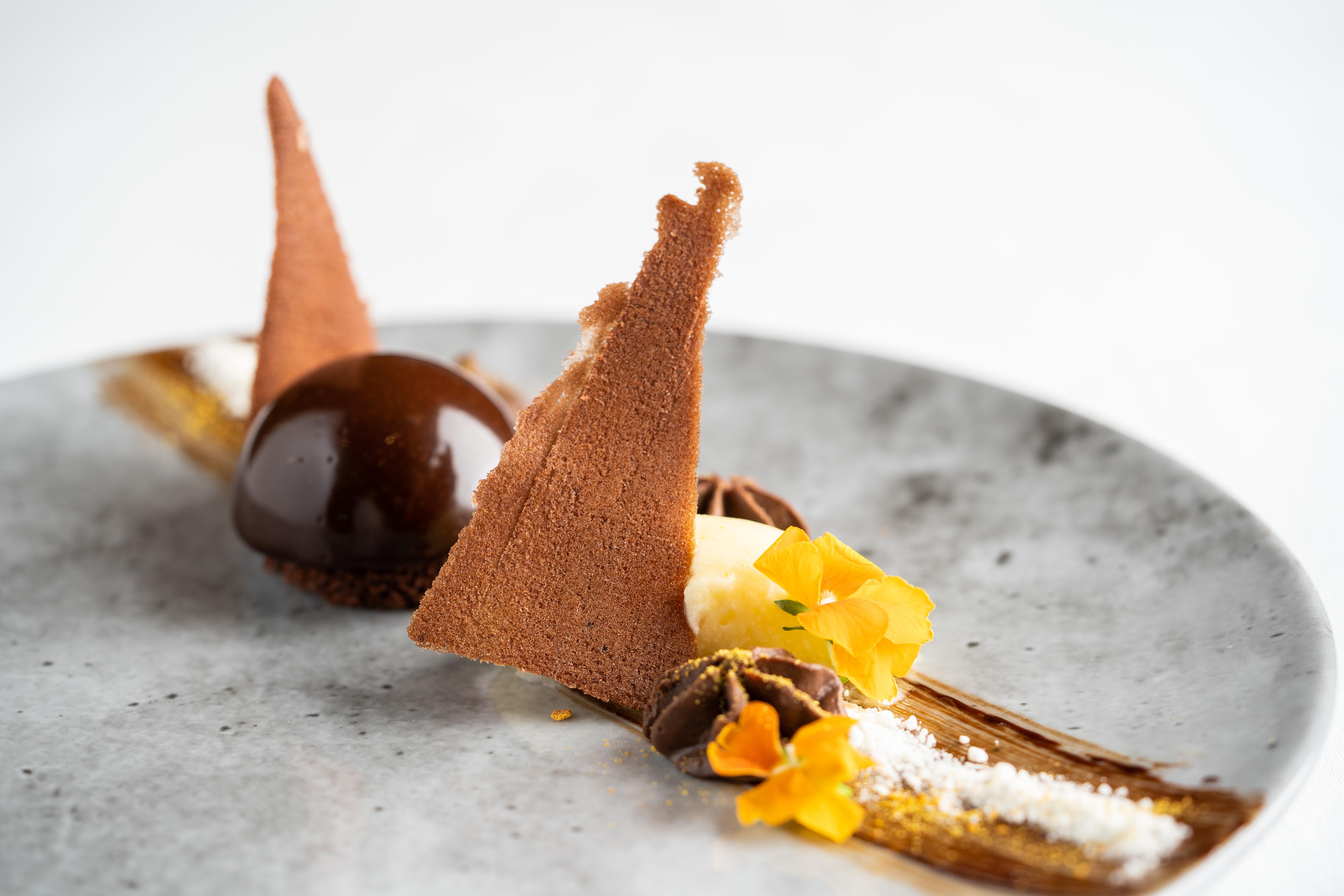 The Fitzwilliam Hotel Belfast Exteriör bild The photo displays an artfully plated dessert. It features a glossy chocolate sphere, accompanied by various chocolate components, including triangular chocolate tuile pieces that resemble sails. The plate is adorned with delicate garnishes such as y