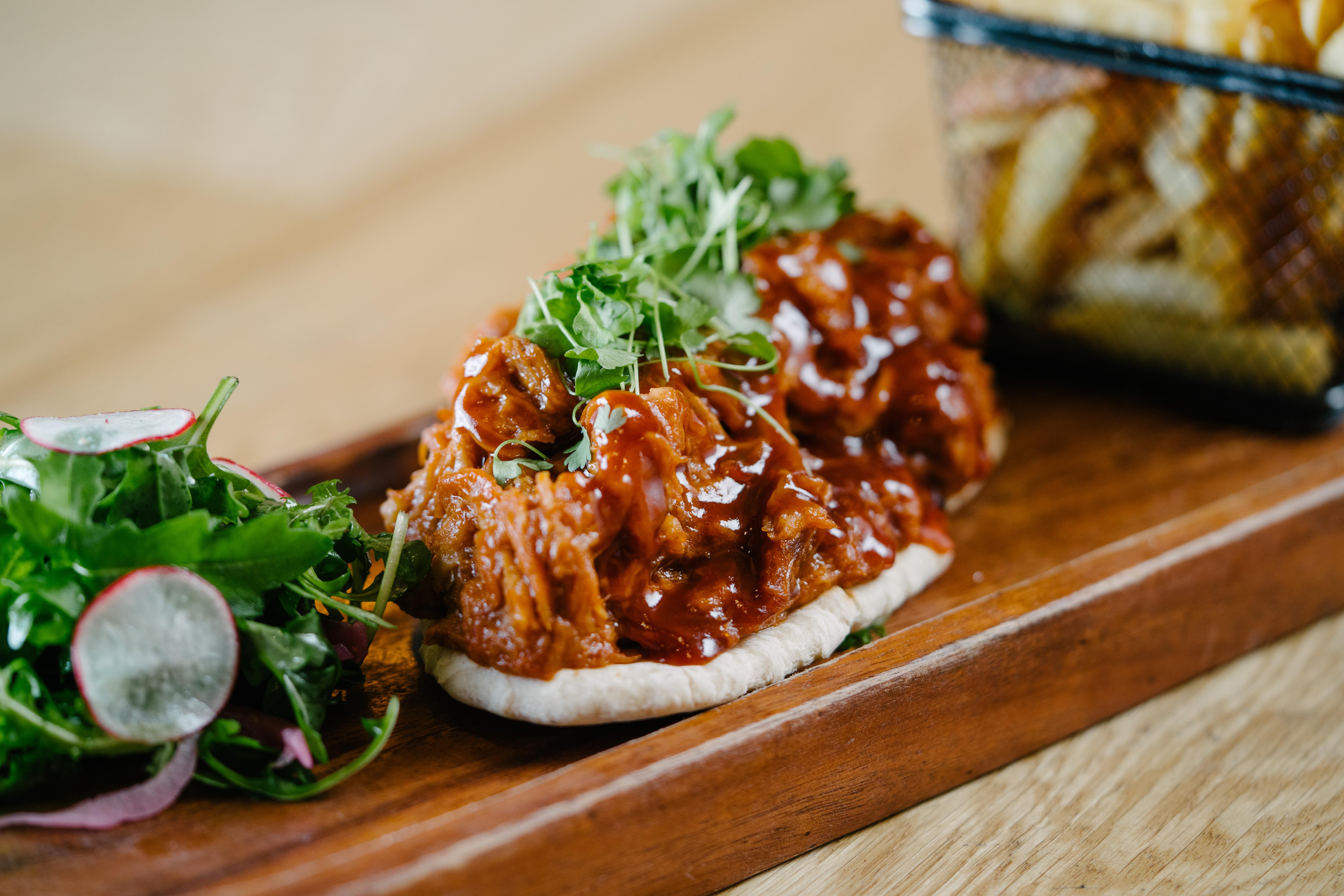 The Fitzwilliam Hotel Belfast Exteriör bild The photo shows a wooden platter featuring two pieces of bread topped with pulled meat covered in a rich barbecue sauce. The dish is garnished with fresh greens, including sprouts. On the side, there is a small serving of mixed salad with radishes an